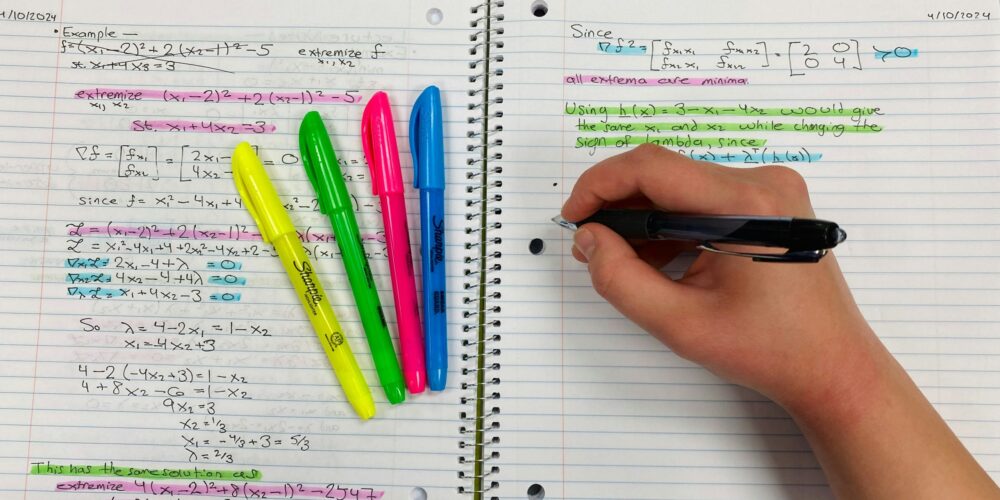Hand writing in a notebook beside colourful highlighters and complex maths notes, symbolising reflective learning and leadership confidence